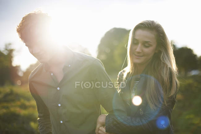 Jovem casal passeando braço a braço no campo iluminado pelo sol — Fotografia de Stock