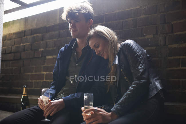 Romantic young couple sitting in bus shelter with prosecco — Stock Photo