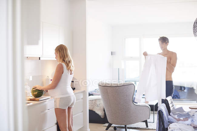 Schwangere junge Frau bereitet Frühstück zu, während Ehemann sich vorbereitet — Stockfoto