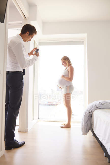 Mann fotografiert schwangere Freundin im Schlafzimmer — Stockfoto