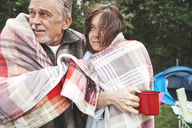 Mature couple wrapped in blanket standing beside tent — Stock Photo