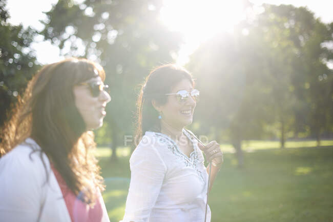 Two mature female friends strolling in sunlit park, London, UK — Stock Photo