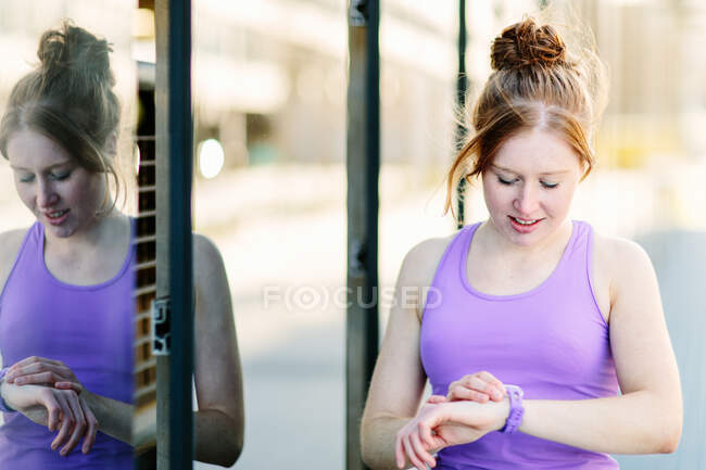 Young female runner looking at smartwatch on city sidewalk — Stock Photo