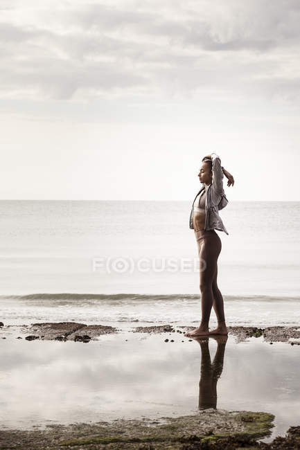 Jeune coureuse sur la plage étirant les bras — Photo de stock