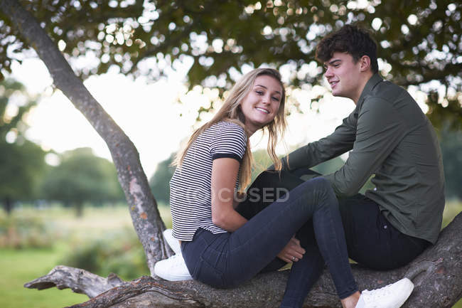 Portrait of young couple sitting on tree branch in field — Stock Photo