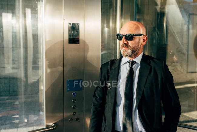 Reifer Geschäftsmann mit Sonnenbrille steht im Fahrstuhl — Stockfoto