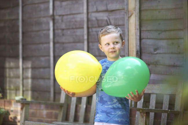 Young boy in garden, holding balloons — Stock Photo