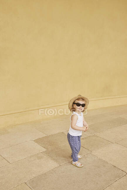 Petite fille debout près du mur jaune — Photo de stock