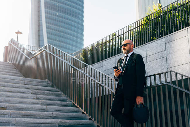 Зрелый бизнесмен стоит на ступеньках со смартфоном — стоковое фото
