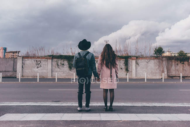 Молода пара, стоячи на дорозі, тримає руки, вид ззаду — стокове фото