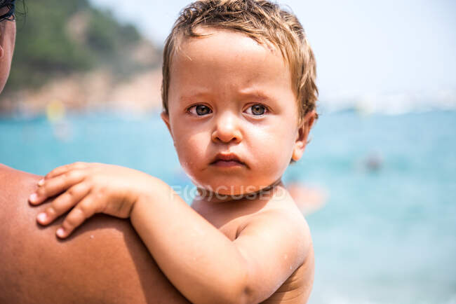Vue de dessus l'épaule de la mère portant un fils mâle tout-petit sur la plage, Begur, Catalogne, Espagne — Photo de stock