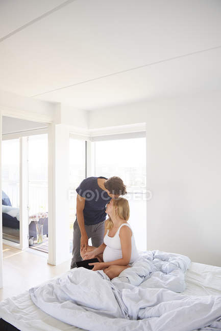 Hombre besando embarazada novia en el dormitorio - foto de stock