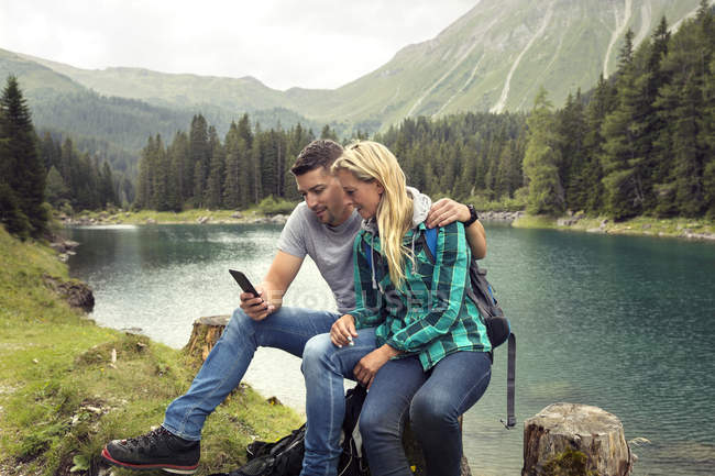 Couple hiking, sitting by lake looking at smartphone, Tirol, Steiermark, Austria, Europe — Stock Photo