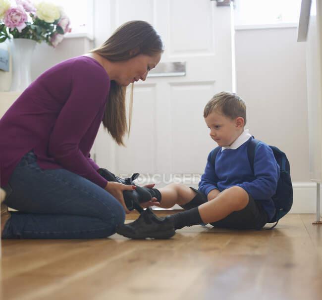 Frau zieht im Hausflur Schuh ihres Sohnes an — Stockfoto