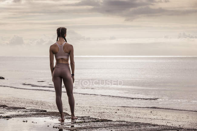 Vista trasera de la joven corredora en la playa mirando al mar - foto de stock