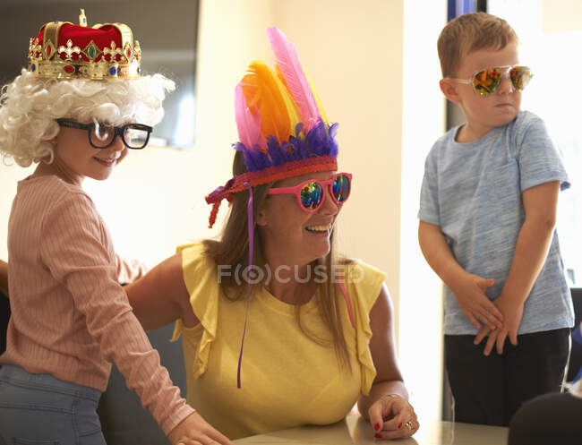 Madre, hijo e hija jugando a disfrazarse, usando sombreros y anteojos divertidos, riendo - foto de stock