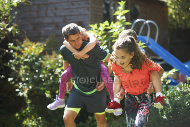 Family playing piggyback race in garden — Stock Photo