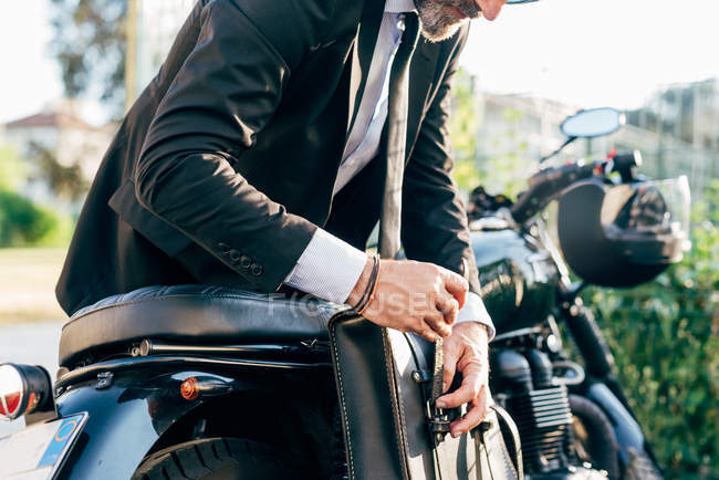 Mature businessman leaning over motorcycle fastening bag — Stock Photo
