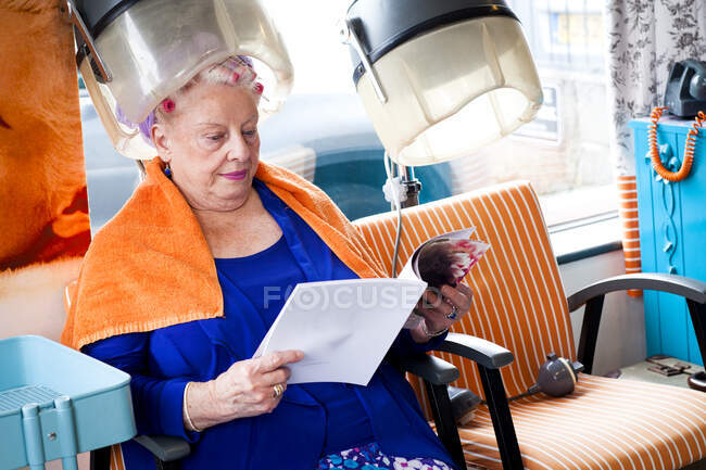 Femme client lecture magazine dans salon de coiffure — Photo de stock