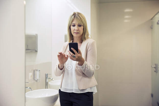 Woman using smartphone in bathroom — Stock Photo