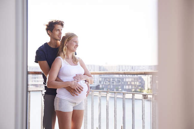 Pregnant couple looking on waterfront from apartment balcony — Stock Photo