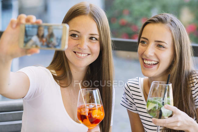 Две юные подружки делают селфи на смартфоне в кафе на тротуаре — стоковое фото