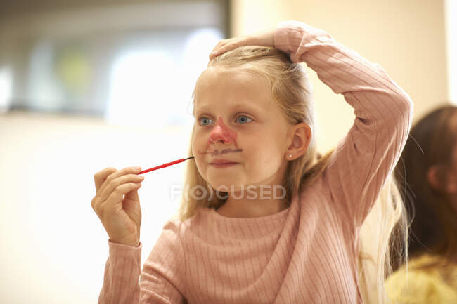 Young girl drawing on her face, using face paint — Stock Photo