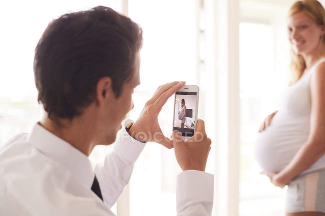 Sobre hombro vista del hombre tomando foto de novia embarazada - foto de stock