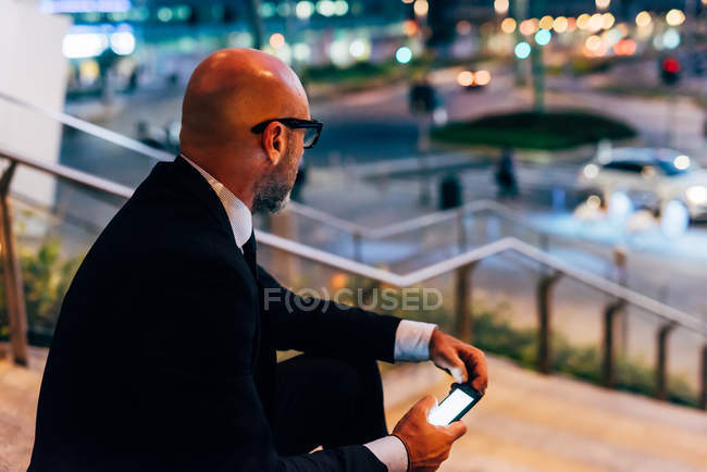 Mature businessman sitting on steps with smartphone — Stock Photo