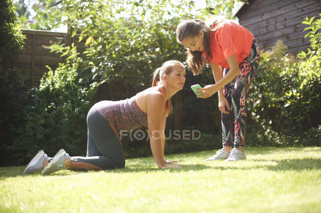 Woman on hands and knees in garden, looking at daughter's smartphone — Stock Photo