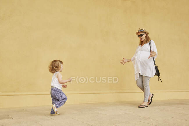 Беременная женщина и дочь играют на жёлтой стене — стоковое фото
