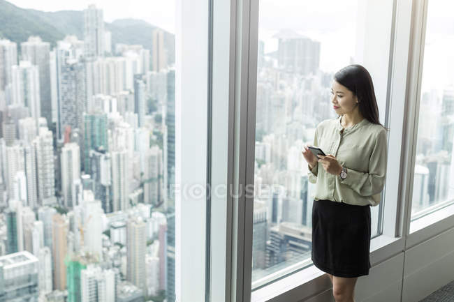Empresária com smartphone olhando pela janela — Fotografia de Stock