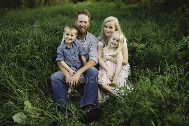 Famille assis ensemble sur l'herbe, regardant la caméra souriant — Photo de stock