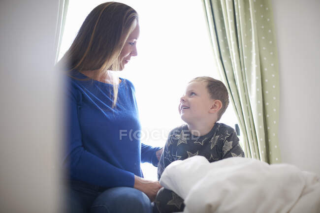 Garçon assis dans le lit bavarder avec la mère — Photo de stock