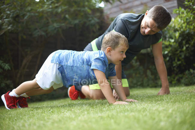 Padre e hijo haciendo ejercicio en el jardín - foto de stock