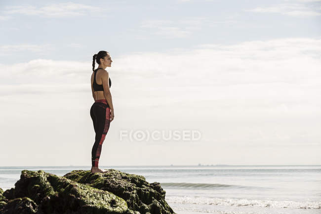 Giovane corridore femminile in piedi su roccia spiaggia — Foto stock