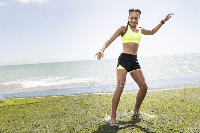 Giovane donna in piedi scalzi su rocce, schizzi in acqua — Foto stock