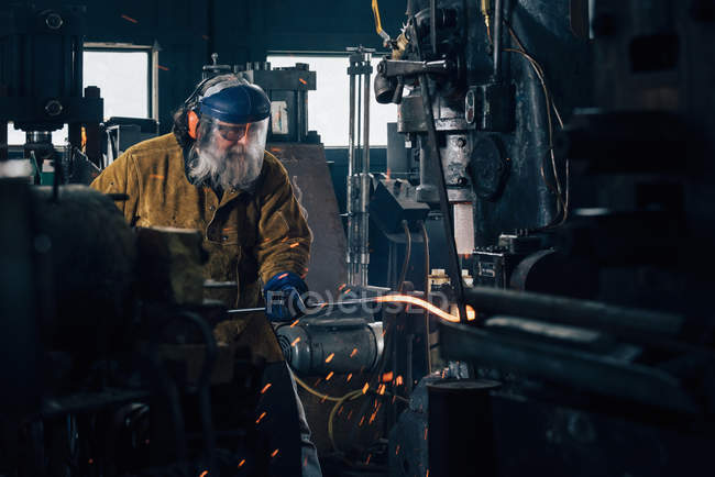 Blacksmith shaping red hot metal rod in workshop — Stock Photo
