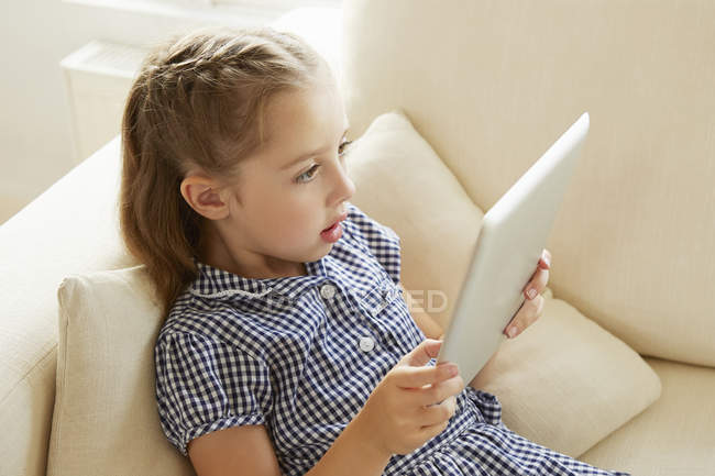 Young girl relaxing on sofa with digital tablet — Stock Photo