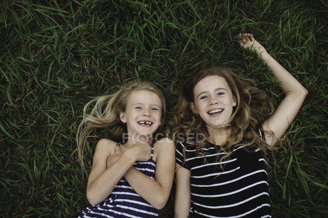 Retrato de arriba de la niña y su hermana acostada en la hierba - foto de stock
