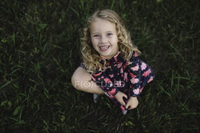 Retrato de arriba de una chica rubia sentada en la hierba - foto de stock