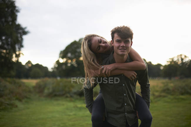 Giovane uomo dando fidanzata a cavalluccio in campo — Foto stock