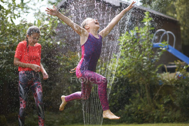 Ragazze che saltano sopra irrigatore giardino — Foto stock