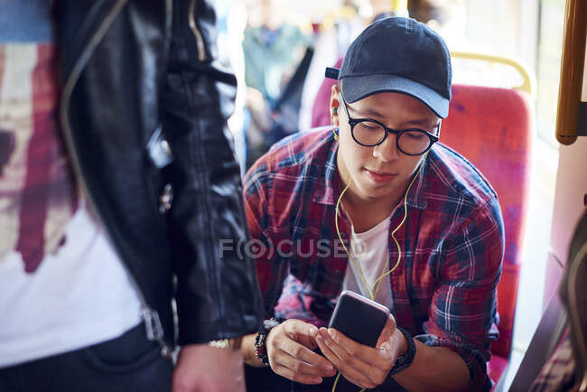 Young man on city tram looking at smartphone and listening to earphones — Stock Photo