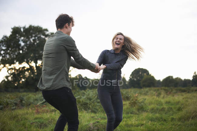 Young couple holding hands and spinning each other around in field — Stock Photo