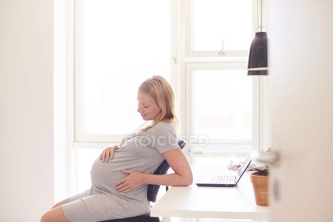 Jovem grávida olhando para o estômago na sala de estar — Fotografia de Stock