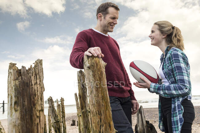 Отец и дочь на пляже, разговаривают, дочь держит регби мяч — стоковое фото