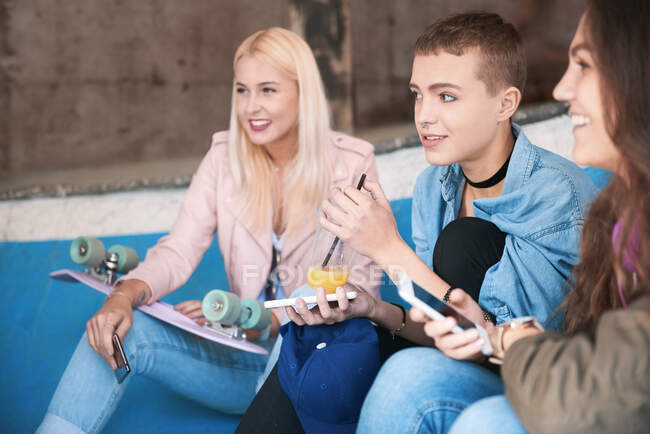 Three young female skateboarding friends with smartphones sitting on skate ramp — Stock Photo