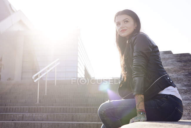 Jeune femme assise sur le mur, regardant ailleurs — Photo de stock