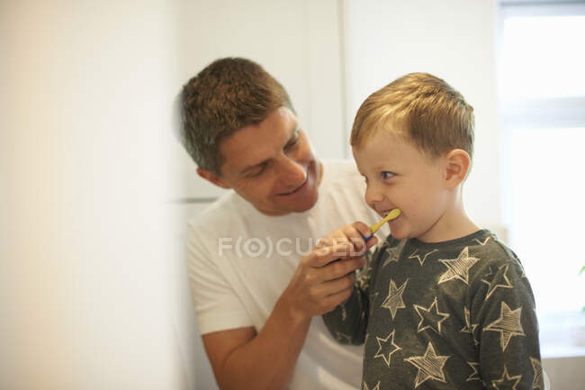 Зрілий чоловік показує синові, як чистити зуби у ванній — стокове фото